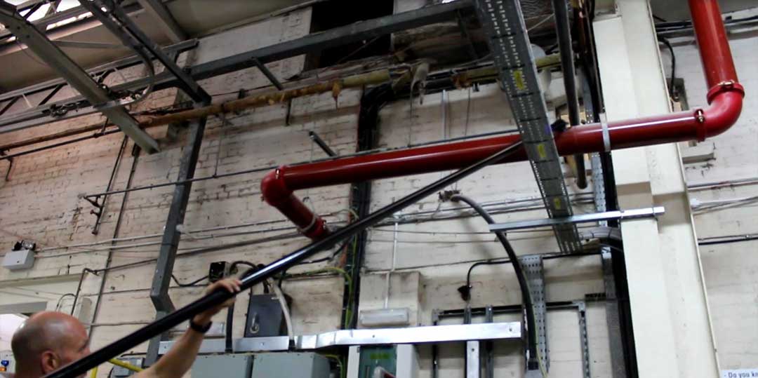 Man using a high-reach vacuum to clean ceiling pipes